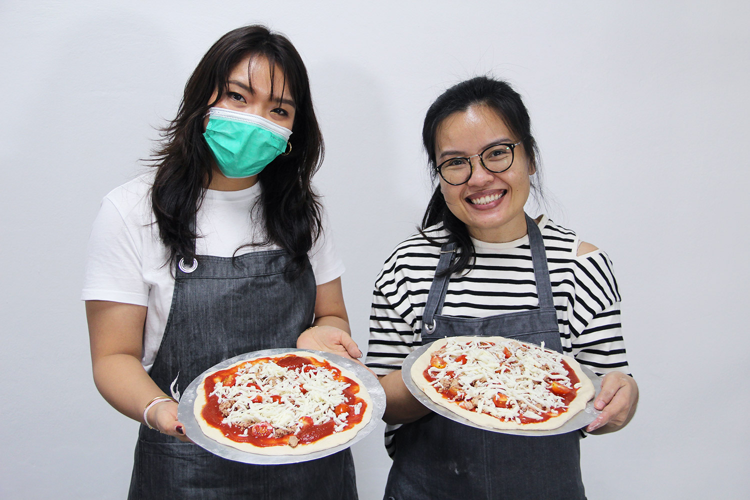 Two students shows their pizza before baking